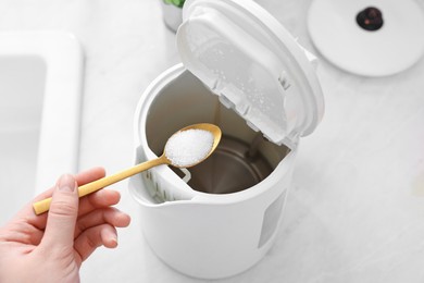 Photo of Cleaning electric kettle. Woman adding baking soda to appliance at table, above view