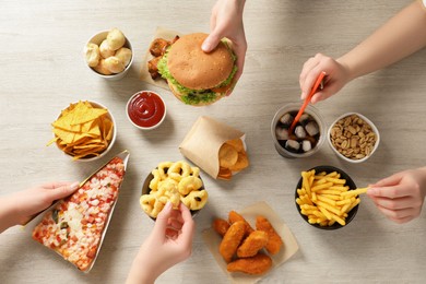 Friends eating french fries, burger and other fast food at white wooden table, top view