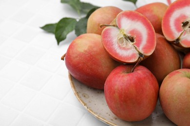 Tasty apples with red pulp and leaves on white tiled table, closeup. Space for text