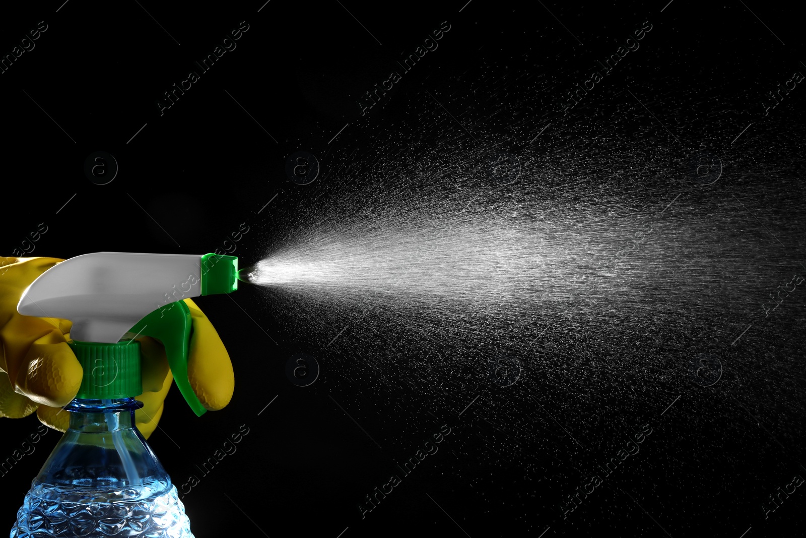 Photo of Woman spraying liquid from bottle on black background, closeup