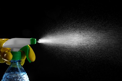 Photo of Woman spraying liquid from bottle on black background, closeup