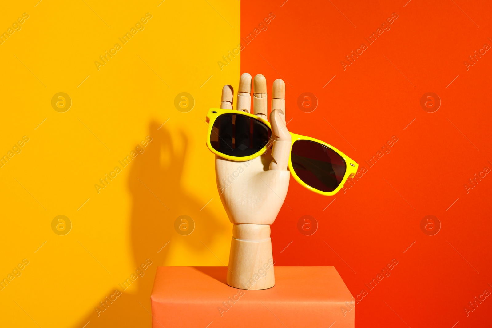 Photo of Wooden mannequin hand with stylish sunglasses on color background