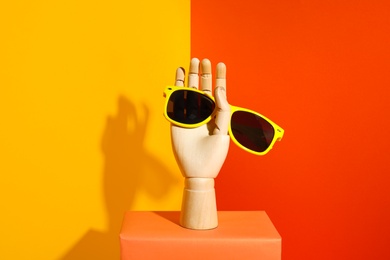 Photo of Wooden mannequin hand with stylish sunglasses on color background