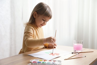 Photo of Cute little girl drawing with brush at wooden table indoors. Child`s art
