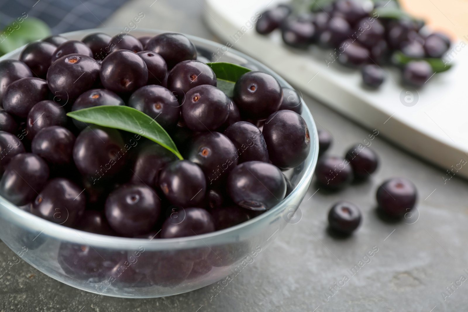 Photo of Fresh acai berries in glass bowl on grey table, closeup