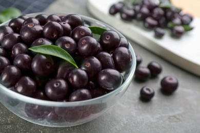 Fresh acai berries in glass bowl on grey table, closeup