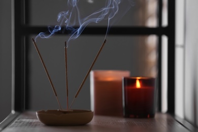 Photo of Incense sticks smoldering on shelf indoors, space for text