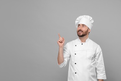Photo of Mature chef pointing at something on grey background, space for text