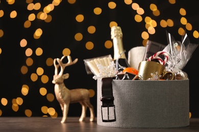 Photo of Basket with Christmas gift set on wooden table against blurred festive lights