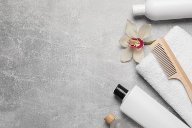Photo of Shampoo bottles, wooden comb, orchid flower and towel on grey table, flat lay. Space for text