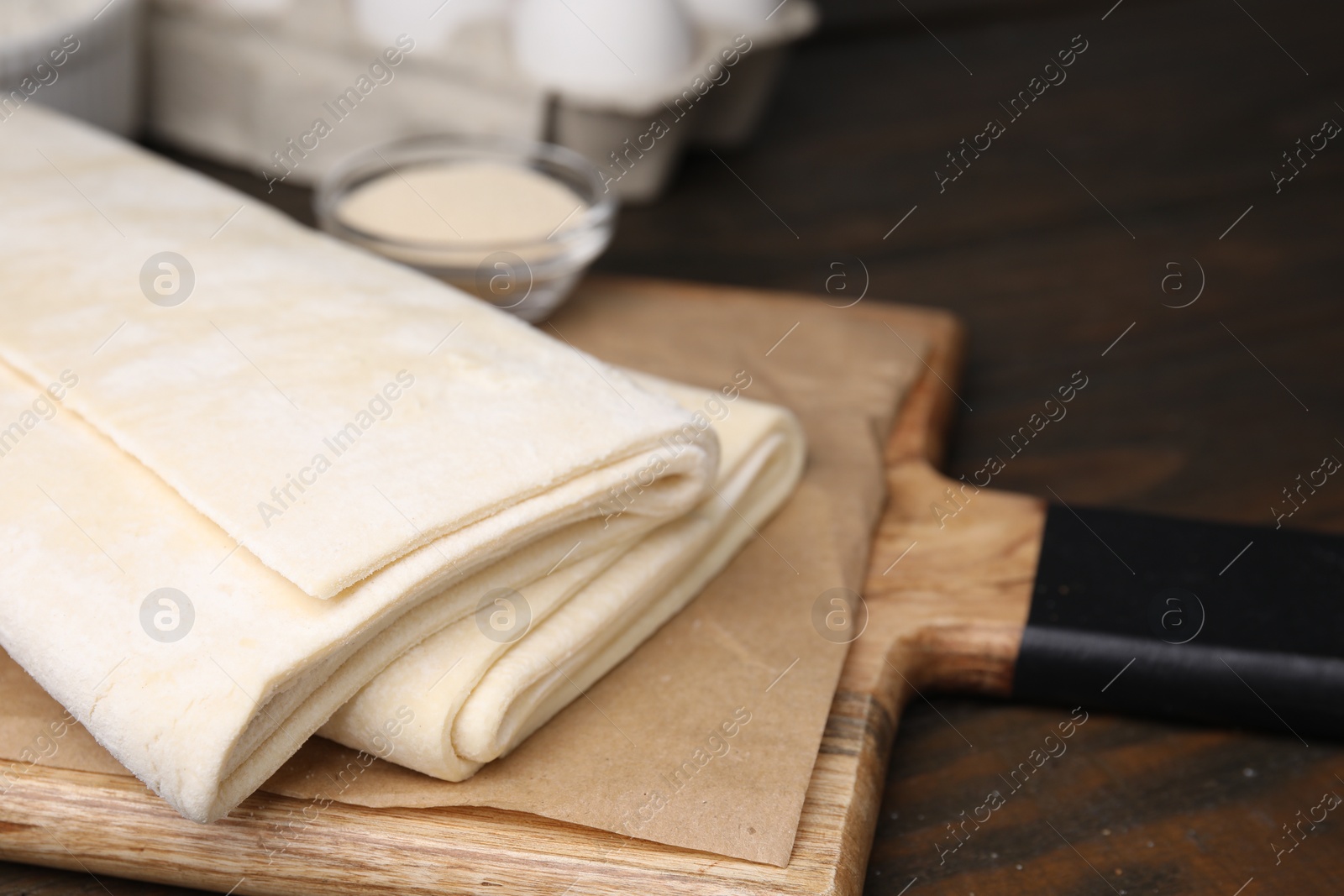 Photo of Raw puff pastry dough on wooden table, closeup