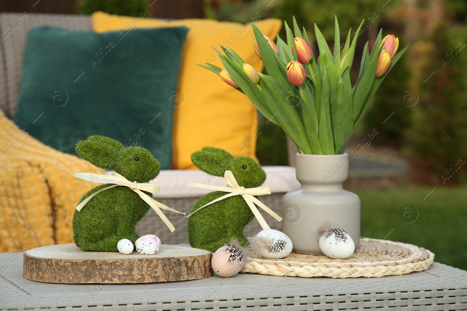 Photo of Terrace with Easter decorations. Bouquet of tulips in vase, bunny figures and decorative eggs on table outdoors