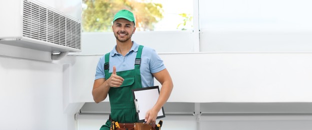 Professional technician with clipboard near modern air conditioner indoors, space for text. Banner design