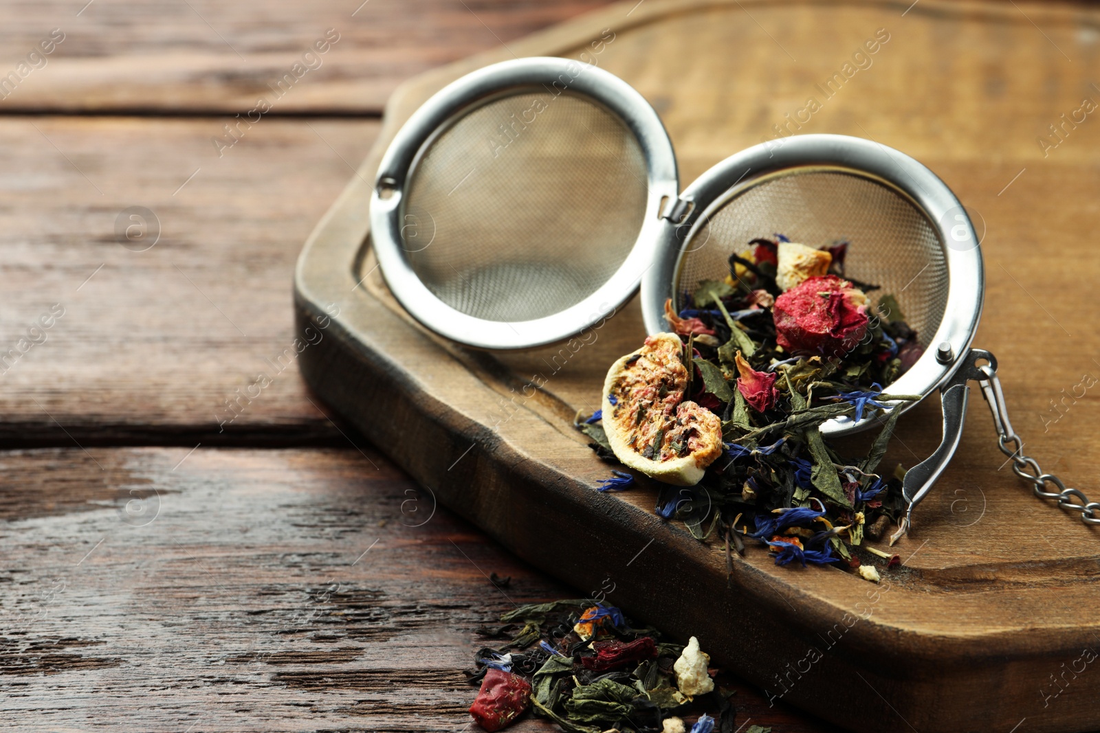 Photo of Snap infuser with dried herbal tea leaves and fruits on wooden table, closeup. Space for text