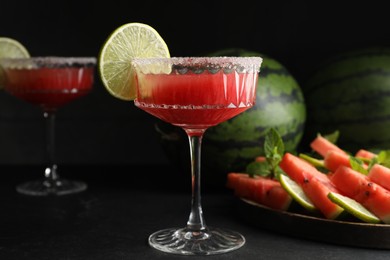 Photo of Cocktail glasses of delicious fresh watermelon juice with lime and sugar rim on black table