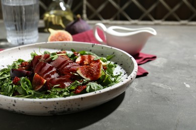 Photo of Plate of tasty bresaola salad with figs, sun-dried tomatoes and balsamic vinegar on grey table, closeup. Space for text