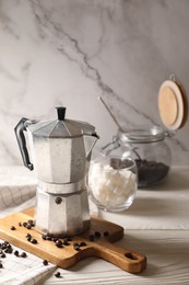 Photo of Moka pot and coffee beans on white wooden table