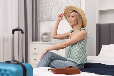 Smiling guest wearing hat relaxing on bed in stylish hotel room