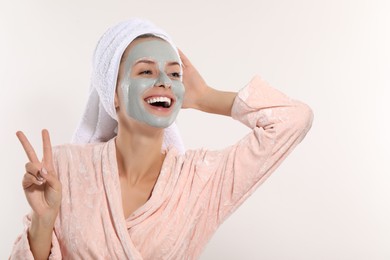 Photo of Woman with face mask showing v-sign on white background, space for text. Spa treatments