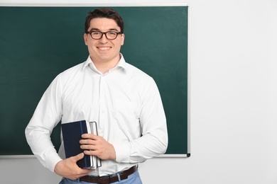 Photo of Portrait of male teacher with notebooks near chalkboard in classroom