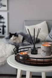Photo of Candles and aroma reed diffuser on white table near grey sofa, closeup