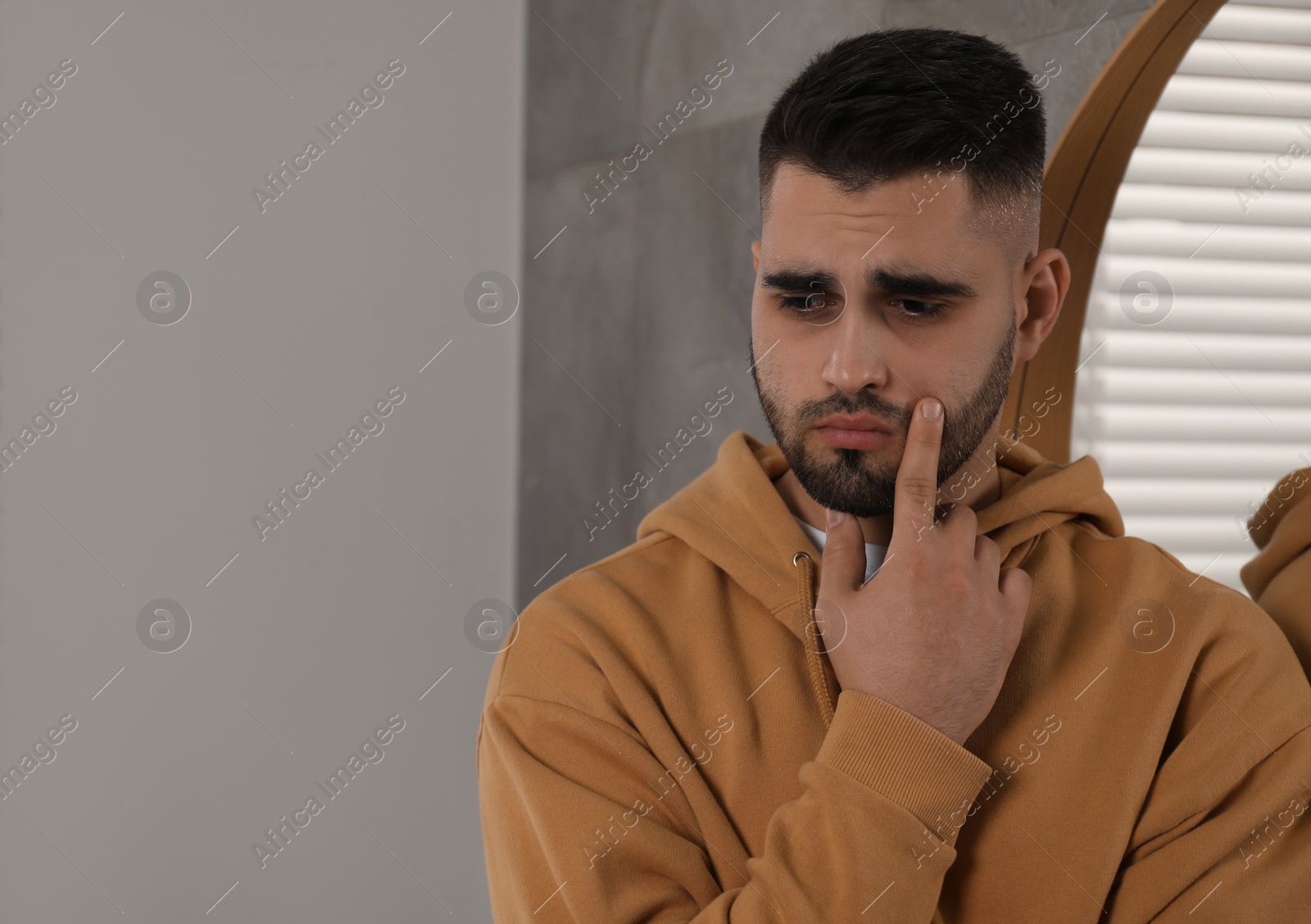 Photo of Sad man near mirror at home. Space for text