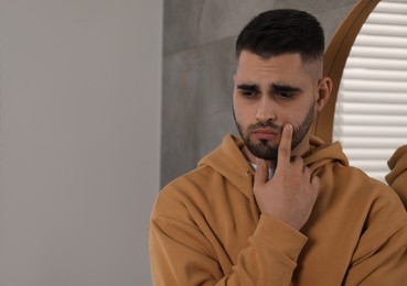 Sad man near mirror at home. Space for text