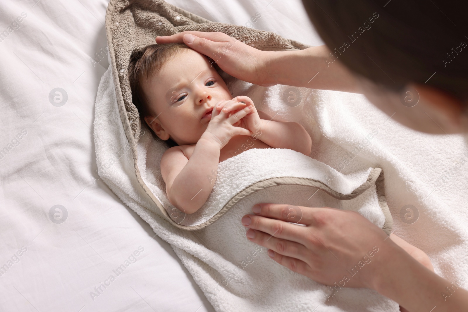 Photo of Mother wrapping her cute little baby with hooded towel after bathing on bed, above view