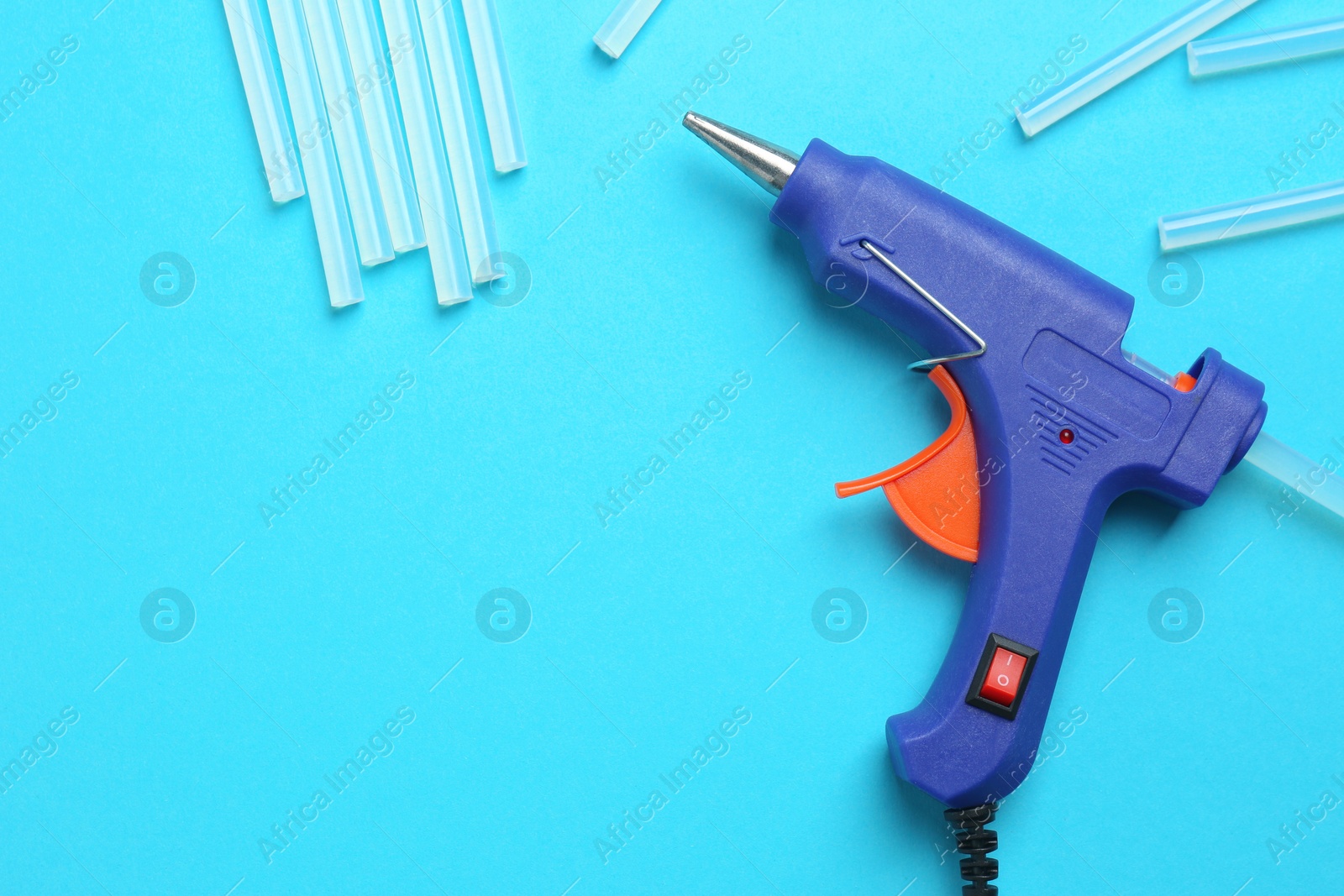 Photo of Glue gun and sticks on light blue background, flat lay. Space for text