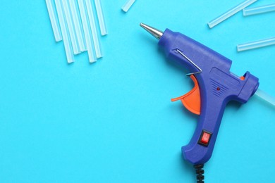 Glue gun and sticks on light blue background, flat lay. Space for text