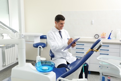 Photo of Portrait of professional male dentist with clipboard in clinic