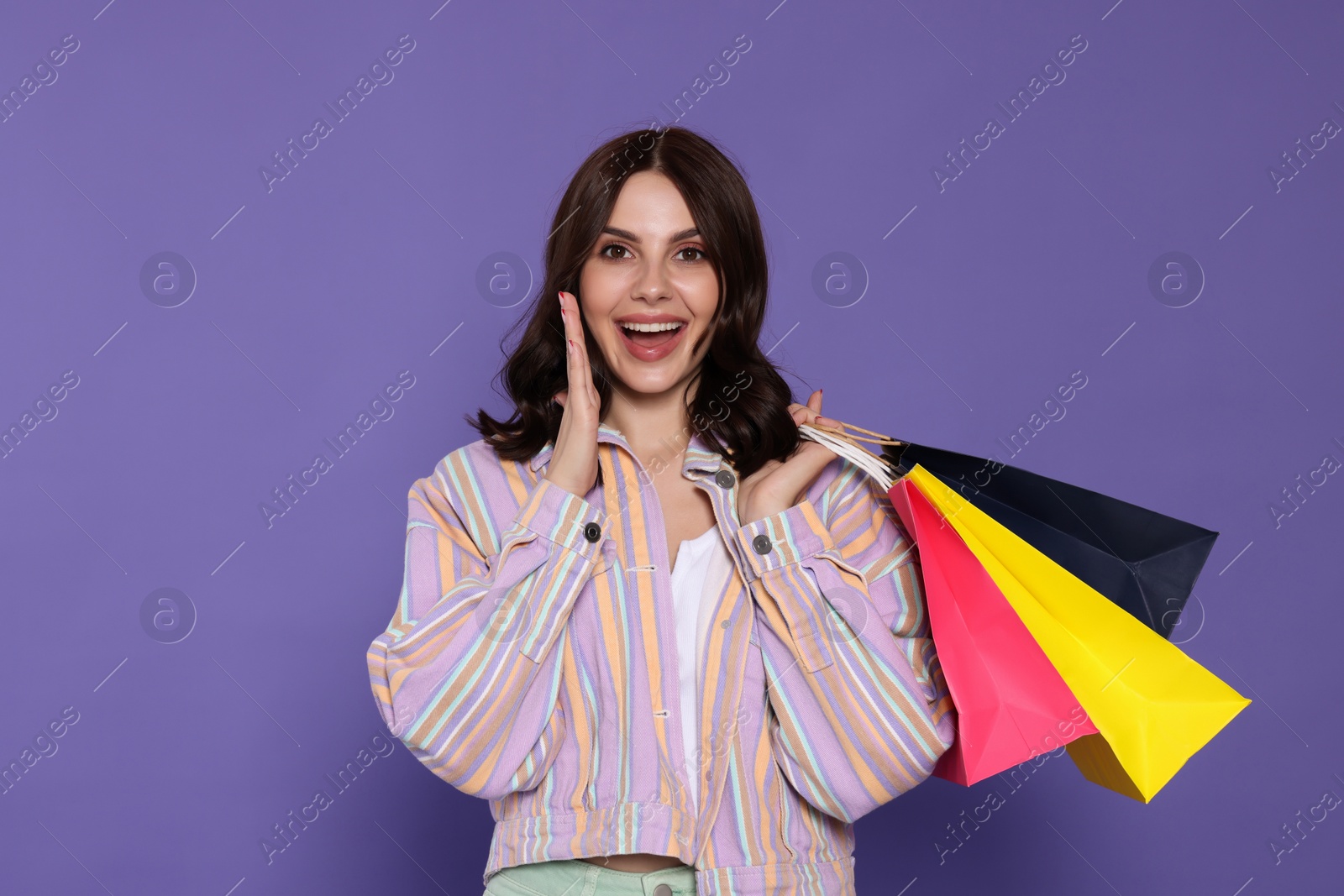 Photo of Emotional young woman with paper shopping bags on purple background