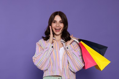 Photo of Emotional young woman with paper shopping bags on purple background