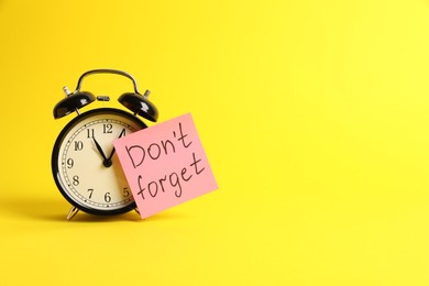 Photo of Alarm clock and reminder note with phrase Don't forget on yellow background, space for text