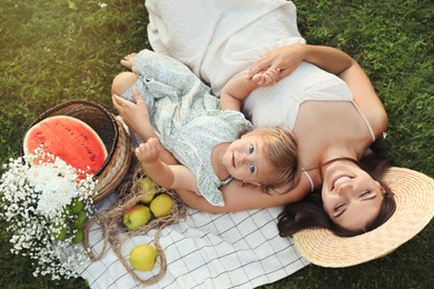 Photo of Mother and her baby daughter resting while having picnic on green grass outdoors, above view