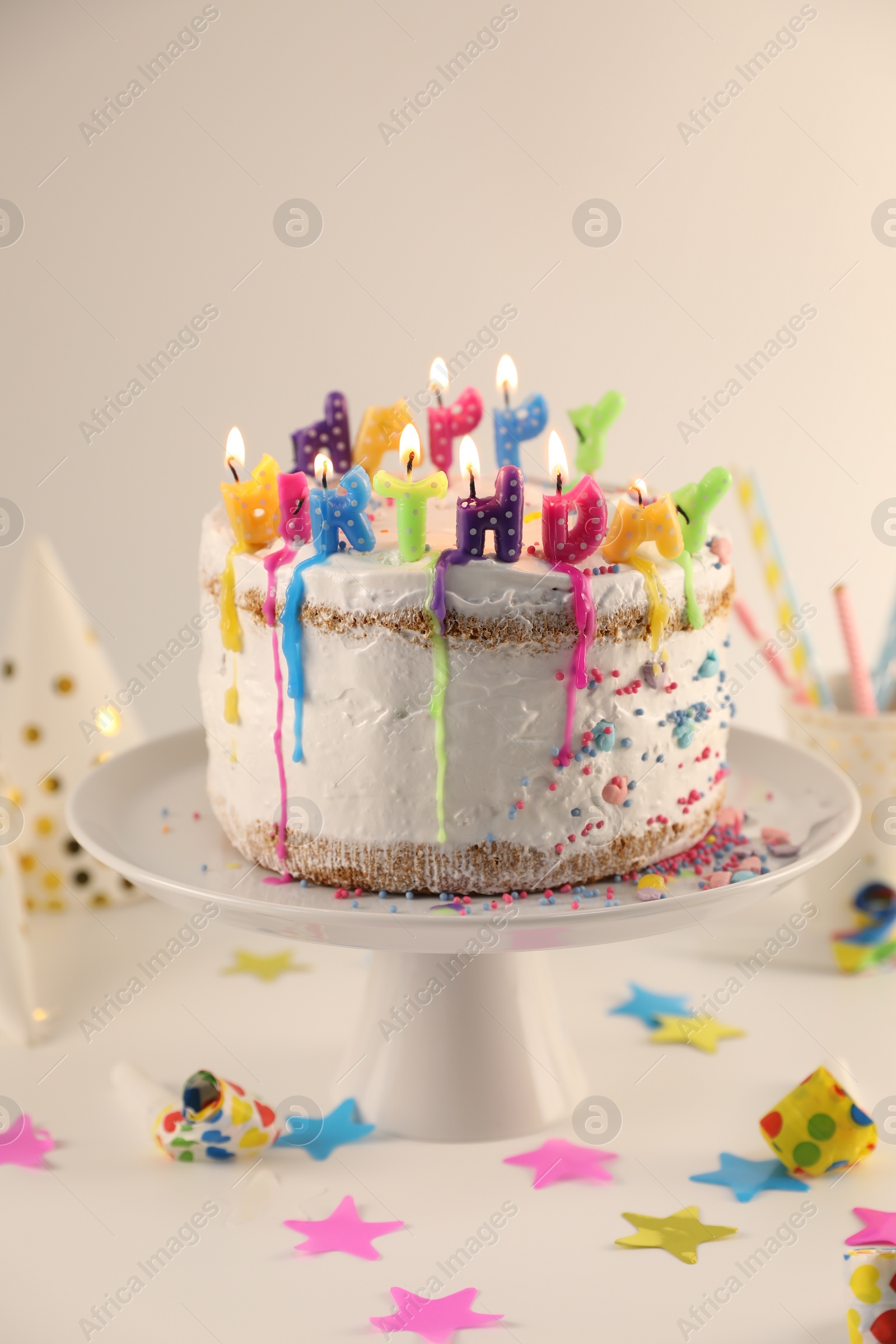 Photo of Tasty Birthday cake with burning candles and party decor on white table