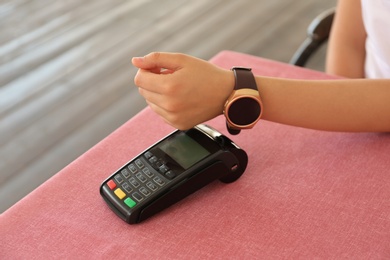 Photo of Woman using smartwatch for contactless payment at table, closeup