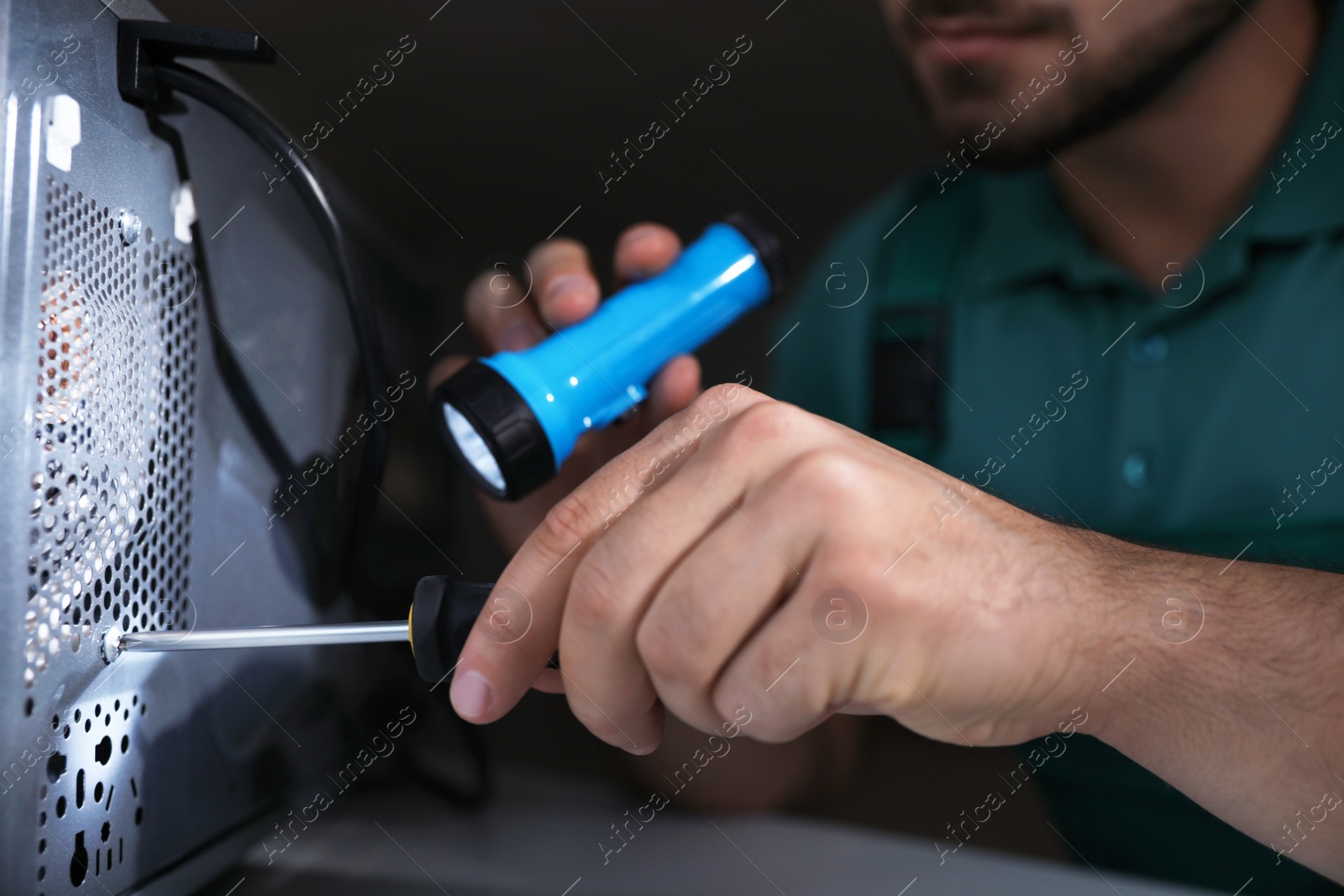 Photo of Repairman with flashlight fixing microwave oven indoors, closeup