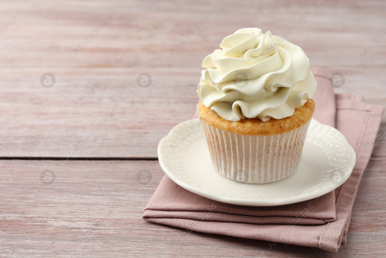 Photo of Tasty cupcake with vanilla cream on pink wooden table, closeup. Space for text