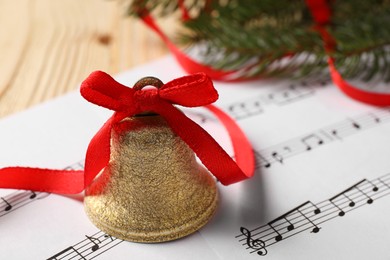 Photo of Golden shiny bell with red bow, music sheets and fir branches on wooden table, closeup and space for text. Christmas decoration
