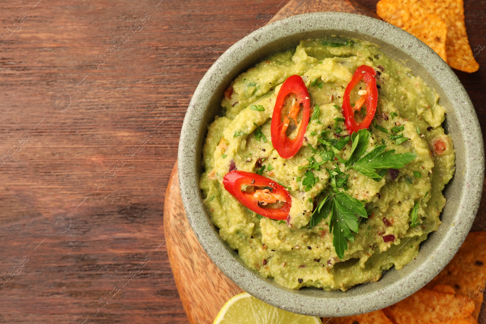 Photo of Bowl of delicious guacamole, lime and nachos chips on wooden table, top view. Space for text