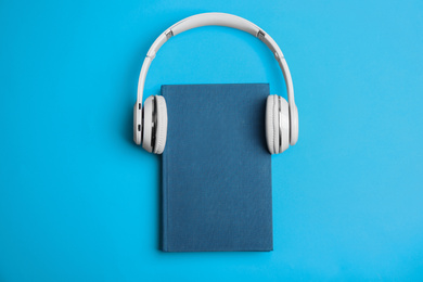 Photo of Book and modern headphones on light blue background, top view