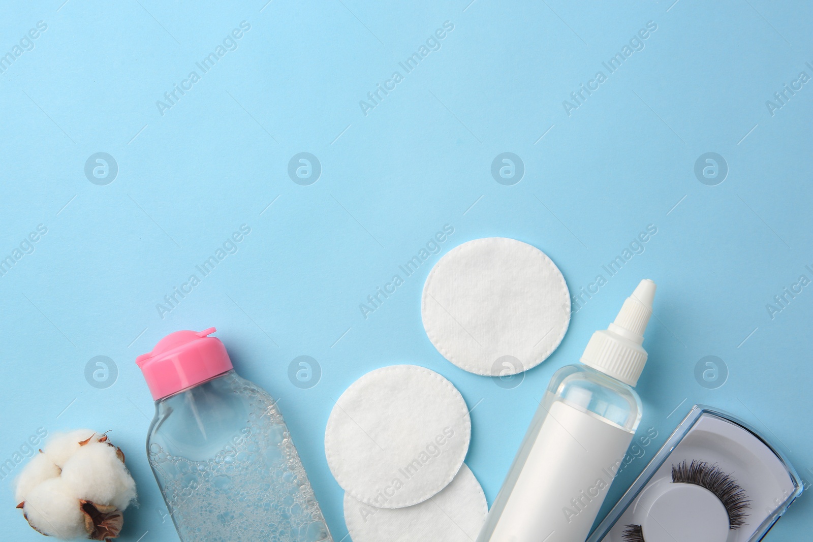 Photo of Bottles of makeup removers, cotton flower, pads and false eyelashes on light blue background, flat lay. Space for text