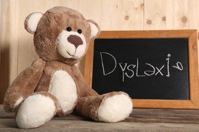 Teddy bear and small blackboard with word Dyslexia on wooden table
