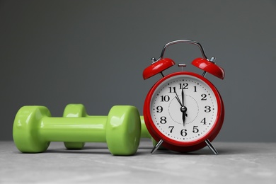 Photo of Alarm clock and dumbbells on table against grey background. Morning exercise