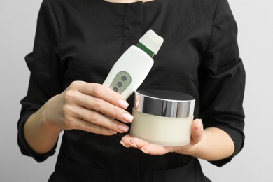 Photo of Cosmetologist with ultrasonic scrubber and jar of cosmetic product on white background, closeup