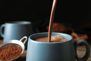 Pouring hot cocoa drink into cup on black background, closeup