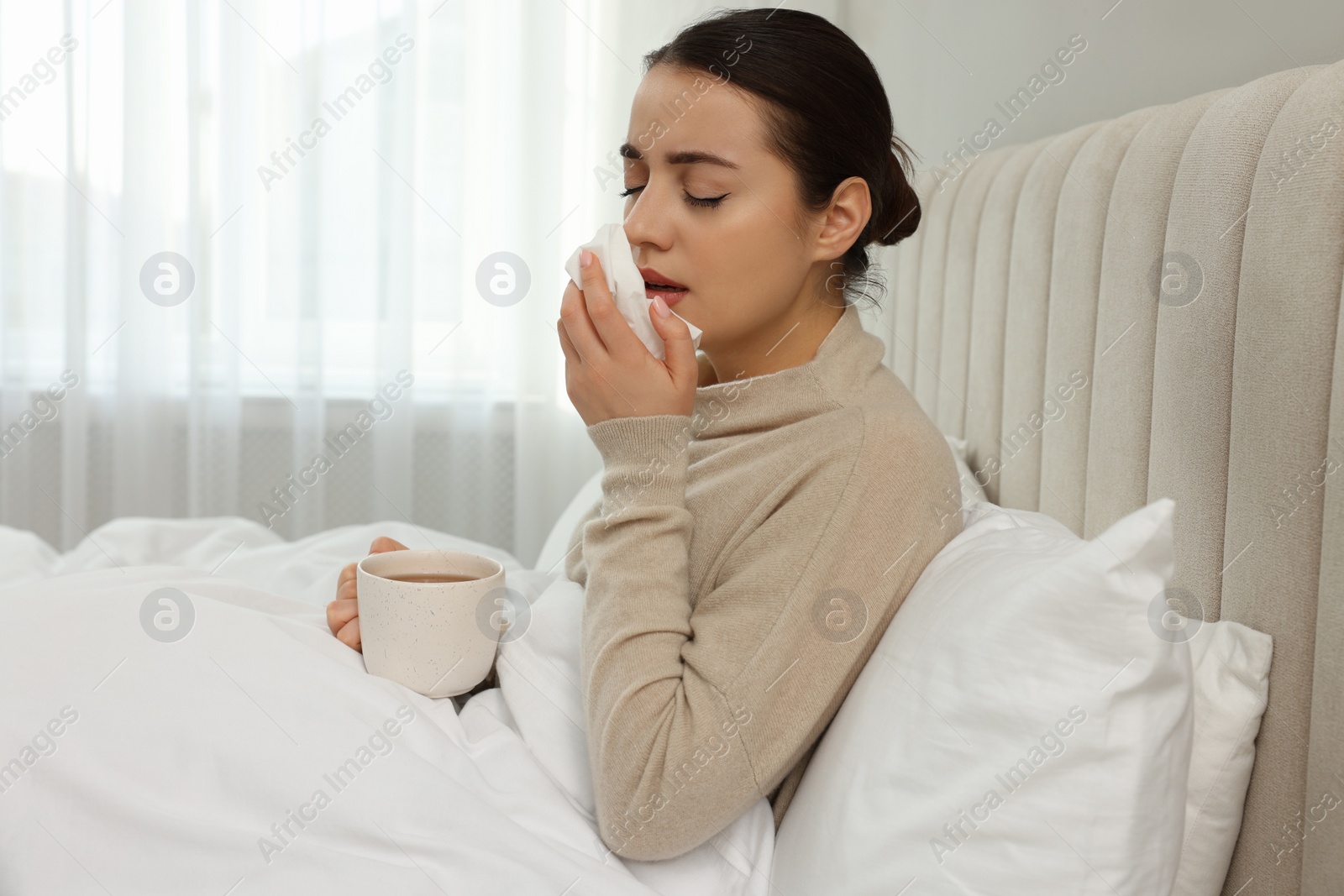 Photo of Sick young woman with cup of hot drink and tissue in bed at home