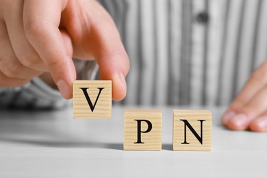 Photo of Woman making acronym VPN with cubes at wooden table, closeup