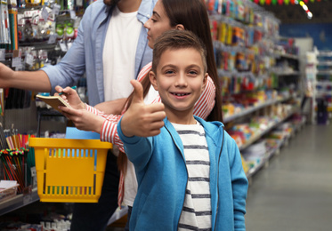 Photo of Little boy with parents choosing school stationery in supermarket